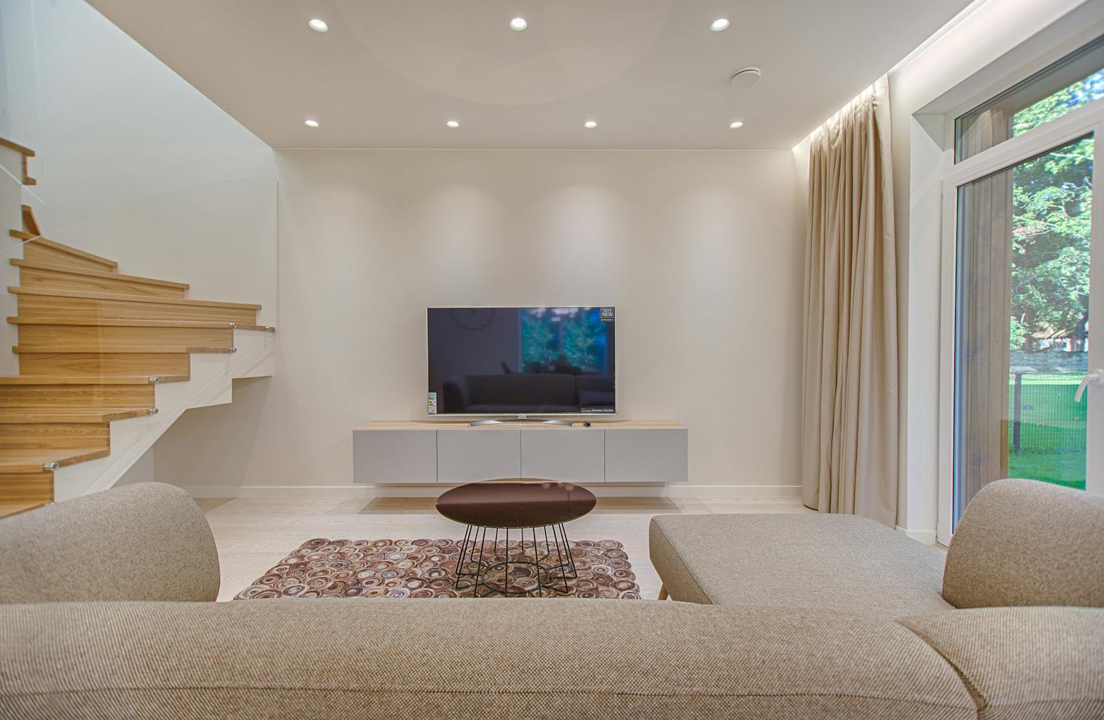 Photo by Vecislavas Popa Contemporary living room with stylish sofa, TV, and staircase, offering a cozy interior design setting.